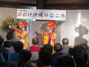 ひびけ沖縄のこころと書かれた横断幕の前で琉球歌舞を踊る2名の写真